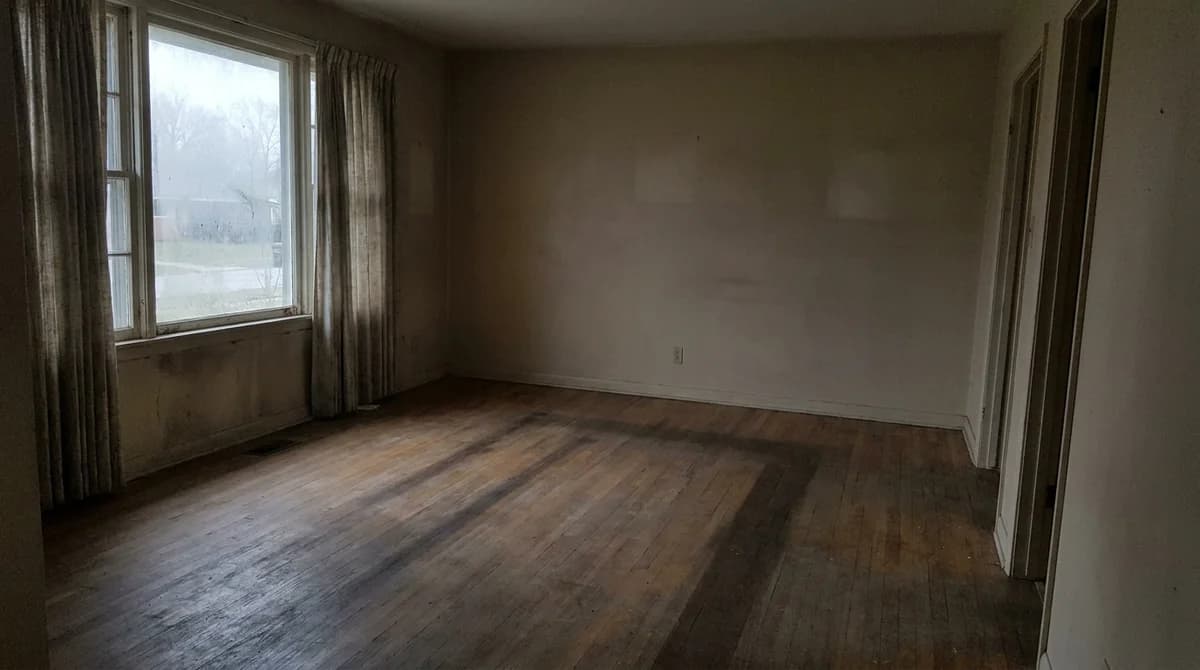 Dull underexposed unedited real estate photo of an empty living room with overcast window light